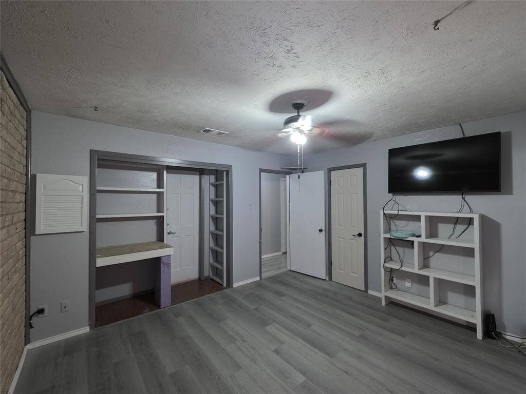 21 W Townhouse Lane, #33, Grand Prairie, TX 75052 Wood-finish flooring, built-in shelving, ceiling fan, and painted brick accent wall