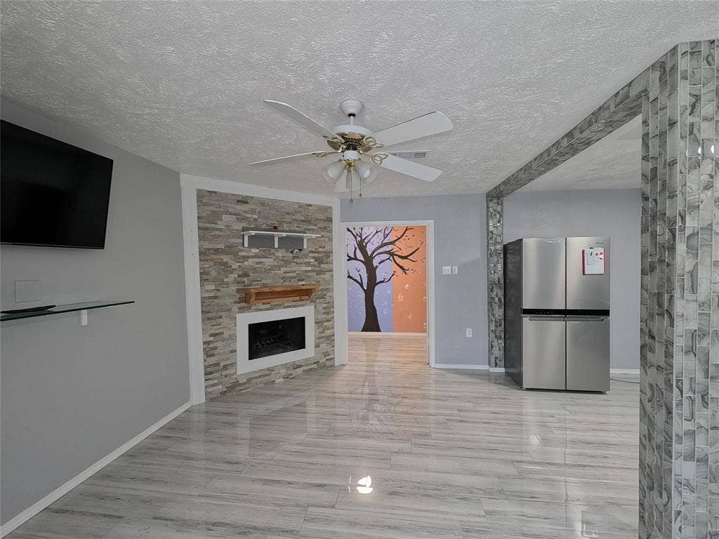 21 W Townhouse Lane, #33, Grand Prairie, TX 75052 Recessed electric fireplace with a wood mantel, stacked stone accent wall, ceiling fan, and wood-finish flooring
