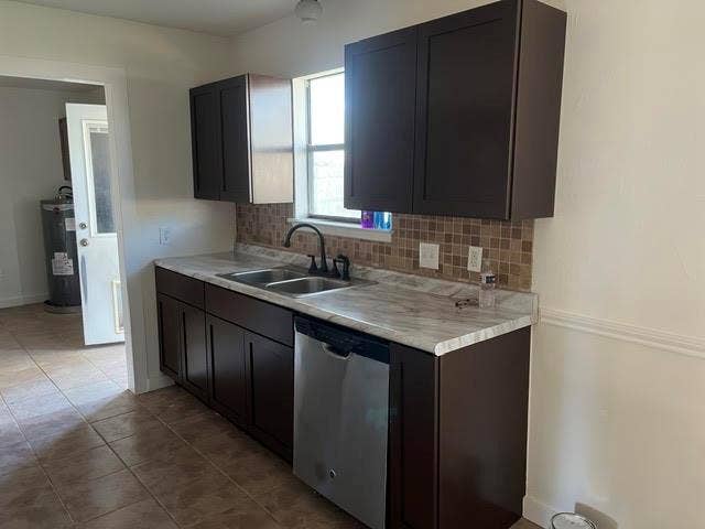 Kitchen featuring dark wood-finish cabinetry, stone-pattern laminate countertops, a mosaic tile backsplash, a dual-basin stainless steel sink with a dark-finish faucet, and a stainless steel dishwasher