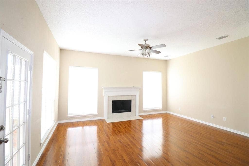 2222 Edinburgh Way, Garland, TX 75040 Vaulted ceiling, wood-finish flooring, fireplace with tile surround, multiple windows, and a ceiling fan with light fixture