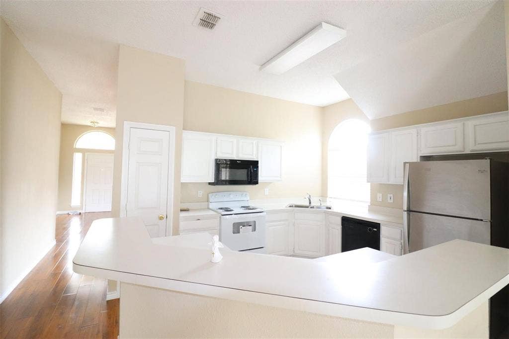 2222 Edinburgh Way, Garland, TX 75040 Kitchen featuring white cabinetry, white countertops, built-in microwave, stainless steel refrigerator, and wood-finish flooring
