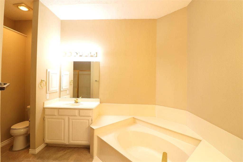 2222 Edinburgh Way, Garland, TX 75040 Corner soaking tub, single vanity with integrated sink, white cabinetry, wall-mounted mirror, and tile flooring