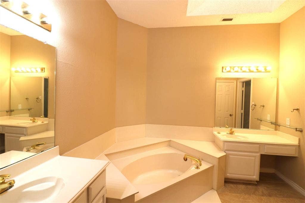 2222 Edinburgh Way, Garland, TX 75040 Soaking tub with gold-tone fixtures, dual vanity sinks, wall-mounted mirrors, and built-in vanity desk