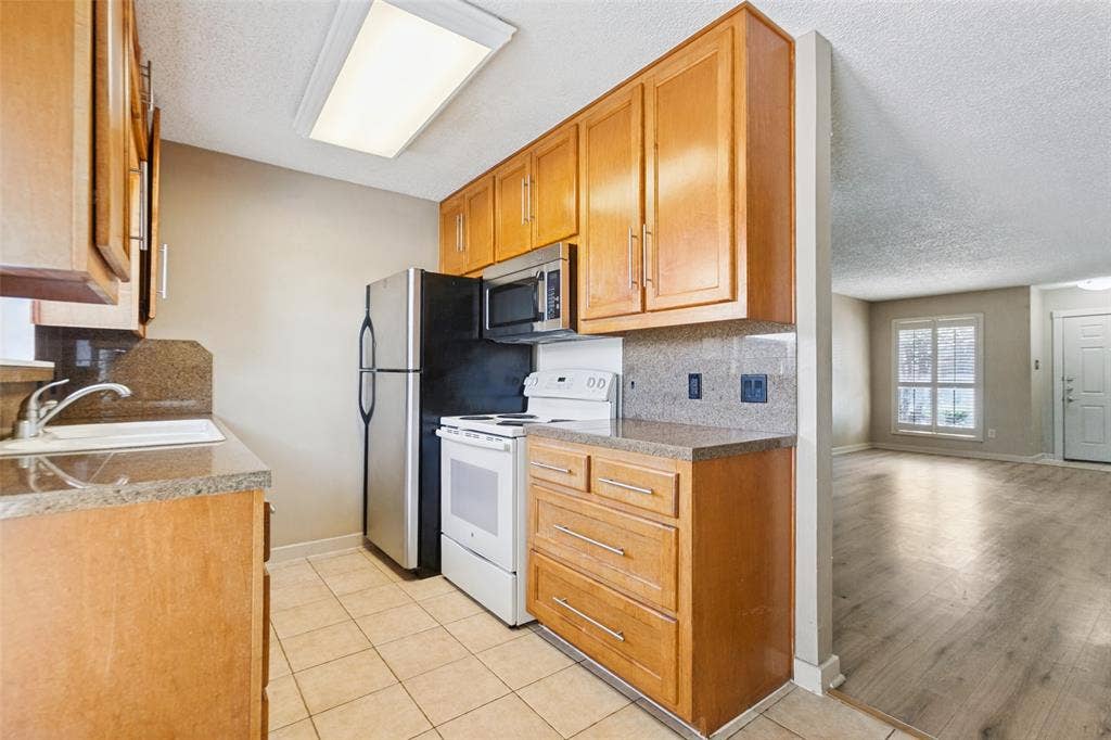 2111 E Belt Line Road, #158B, Richardson, TX 75081 Kitchen featuring wood cabinetry, stone countertops, tile flooring, stainless steel refrigerator, and integrated sink