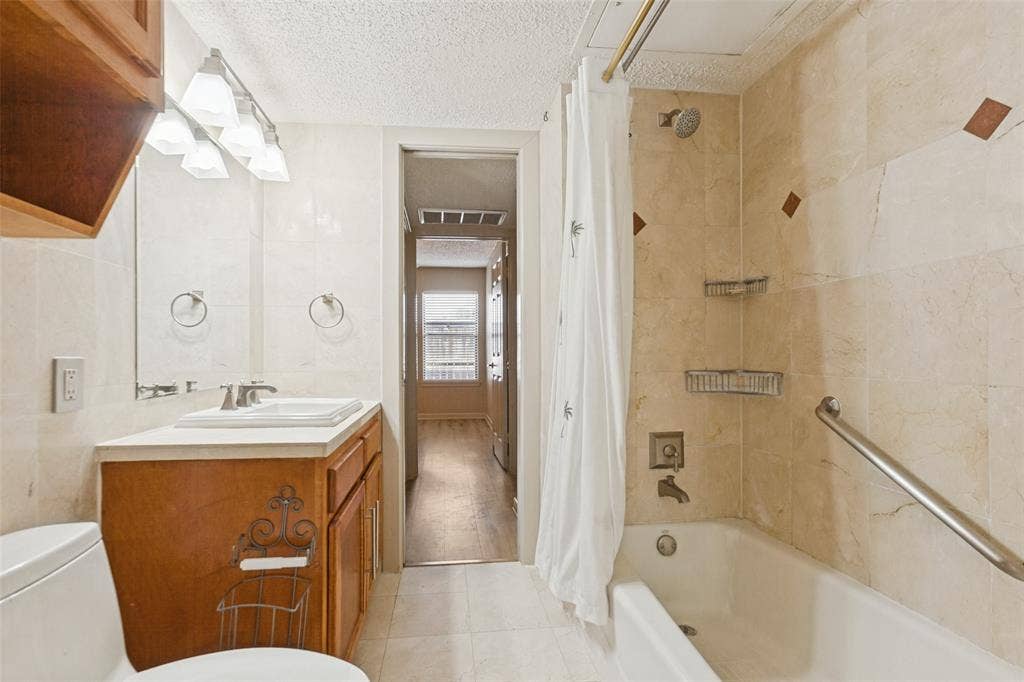 2111 E Belt Line Road, #158B, Richardson, TX 75081 Tile flooring, wood-finish vanity with a built-in sink, wall-mounted mirror, and a tiled shower/tub combination with a grab bar