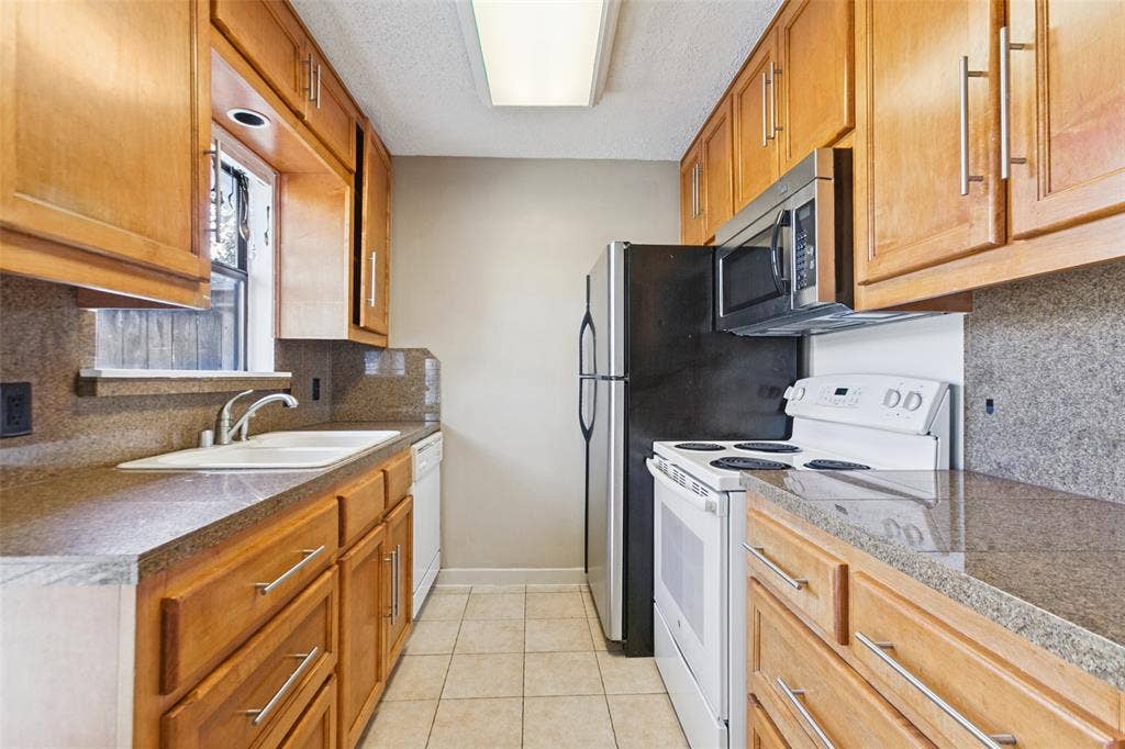 2111 E Belt Line Road, #158B, Richardson, TX 75081 Galley kitchen featuring wood cabinetry, stone-finish countertops, tiled flooring, an undermount sink, and stainless steel appliances