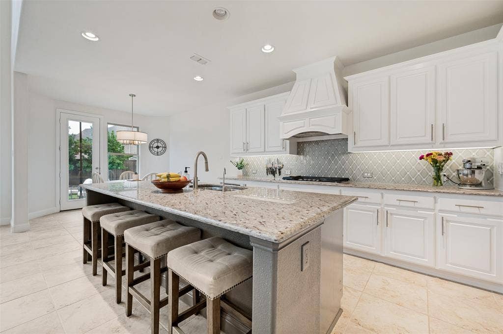 131 Darian Drive, Prosper, TX 75078 Kitchen featuring an expansive island with granite countertop, white cabinetry with under-cabinet lighting, a patterned tile backsplash, and tile flooring