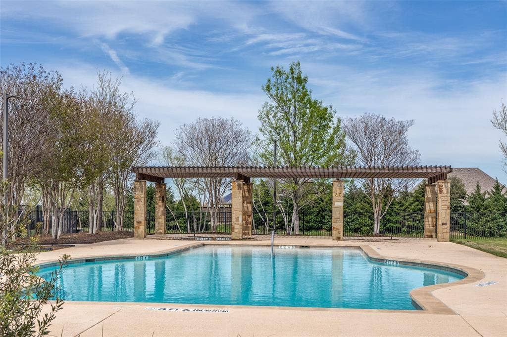 131 Darian Drive, Prosper, TX 75078 Curved swimming pool with concrete decking, stone-columned pergola, and surrounding mature trees