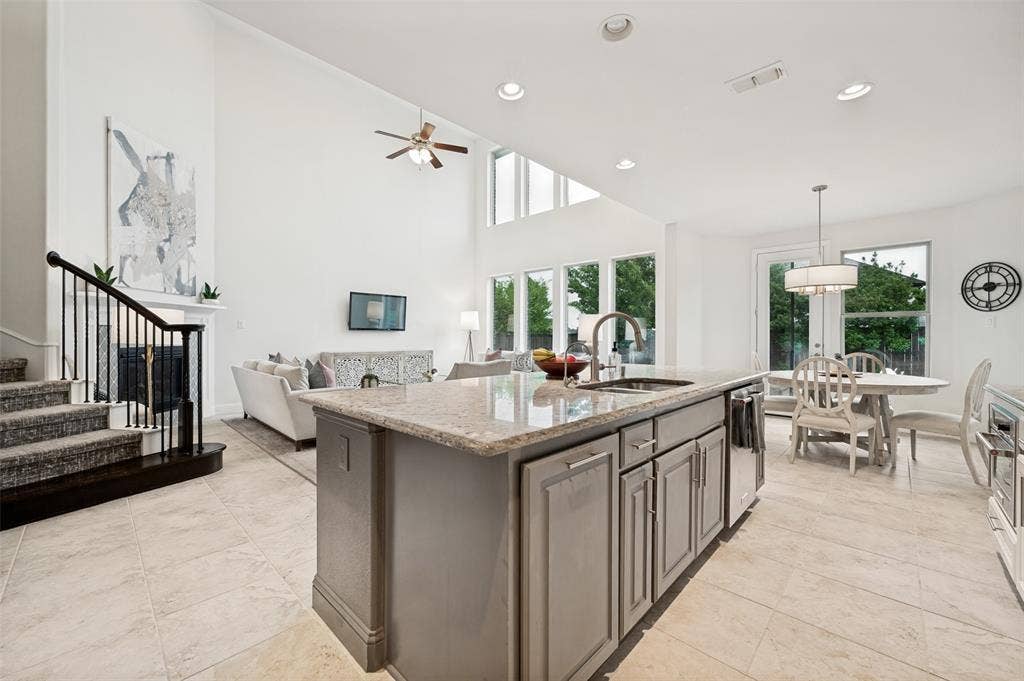 131 Darian Drive, Prosper, TX 75078 Open-concept living space featuring high ceilings, a kitchen island with stone countertop, tile flooring, and a fireplace with a mantel