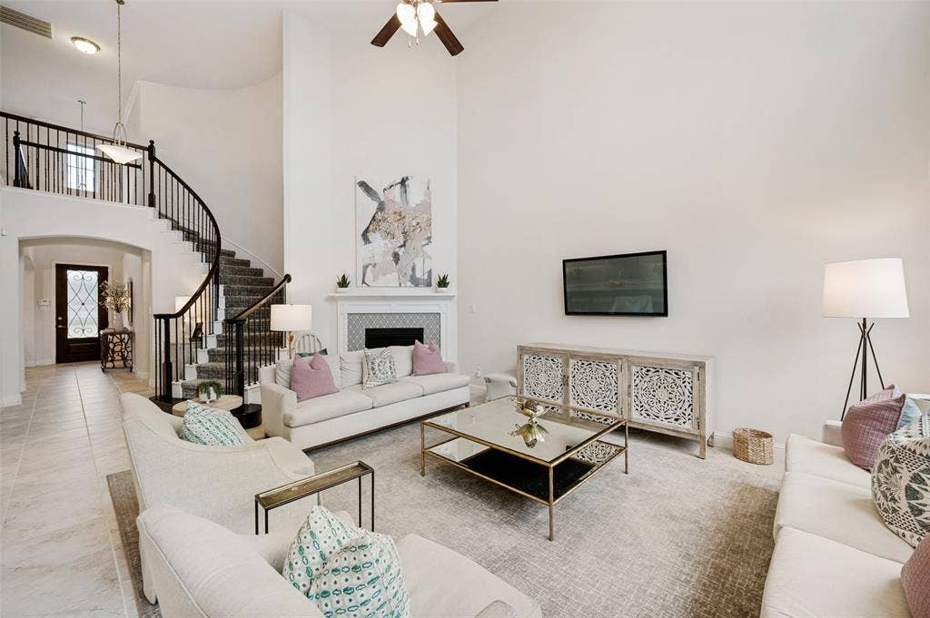 131 Darian Drive, Prosper, TX 75078 Two-story living area featuring a fireplace with decorative tile surround and mantel, curved staircase with metal spindles, and a ceiling fan
