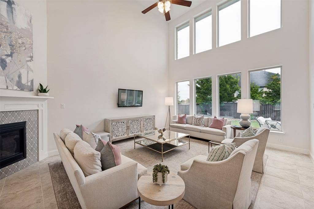 131 Darian Drive, Prosper, TX 75078 Two-story living area with high ceilings, fireplace with decorative tile surround, built-in media console, and a series of tall windows