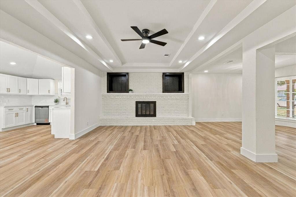 Expansive living area featuring coffered ceilings, wood-finish flooring, a white brick fireplace, and recessed lighting