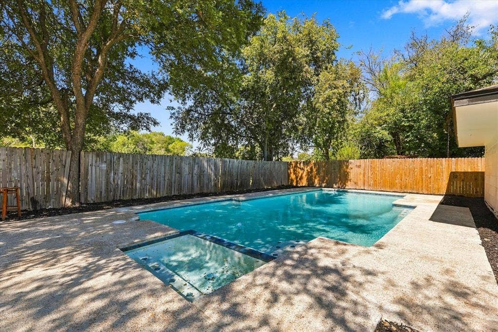 Expansive backyard with a rectangular swimming pool, concrete patio, and a wood privacy fence