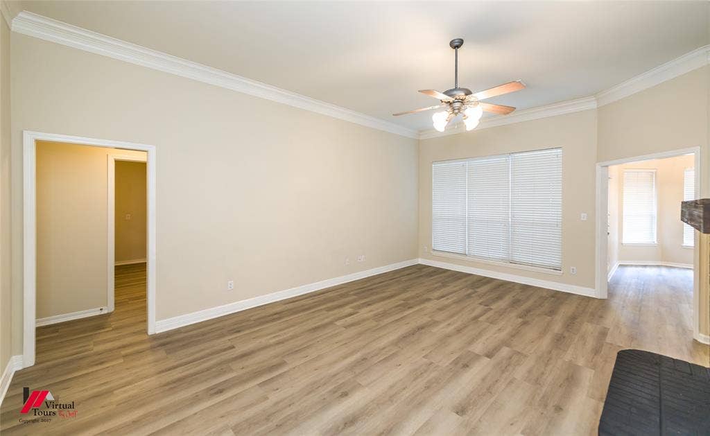 Interior space featuring wood-finish flooring, crown molding, a central ceiling fan with integrated lighting, and multiple windows fitted with horizontal blinds