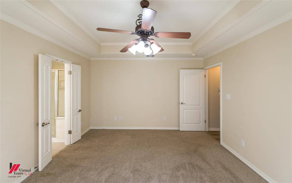 Tray ceiling with crown molding, center-mounted ceiling fan with multi-light fixture, neutral carpeting, and multi-panel interior doors