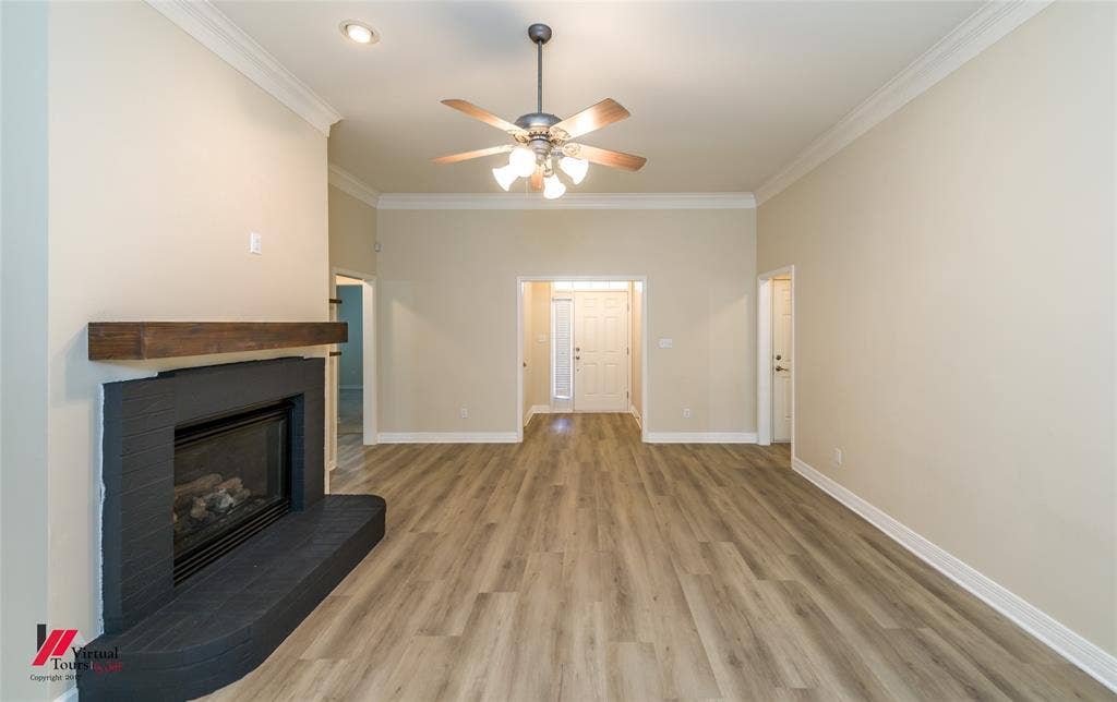 Living area featuring wood-finish flooring, a fireplace with a black tile surround and wood mantel, recessed lighting, and crown molding