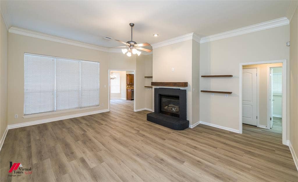 Living area featuring wood-finish flooring, a fireplace with a black surround, a floating wood mantel, crown molding, and built-in floating shelves