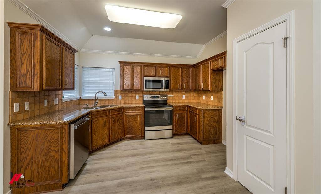 Kitchen featuring wood cabinetry, stone countertops, square tile backsplash, stainless steel appliances, and wood-finish flooring