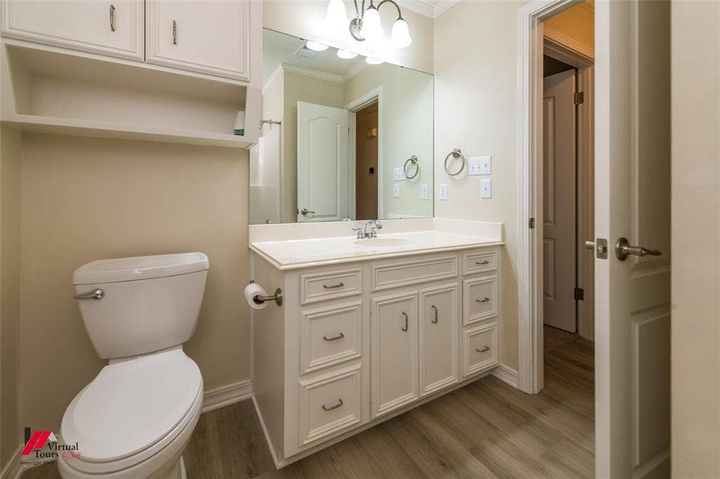 Bathroom featuring a white vanity cabinet with drawers, integrated countertop with sink, large wall-mounted mirror, and wood-finish flooring