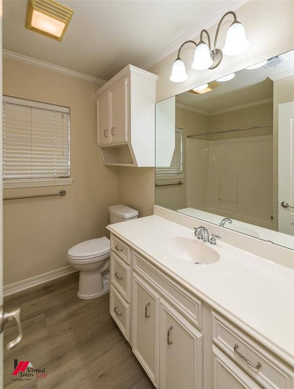 Bathroom featuring a vanity with white cabinetry, integrated sink, large wall-mounted mirror, overhead three-light fixture, and wood-finish flooring