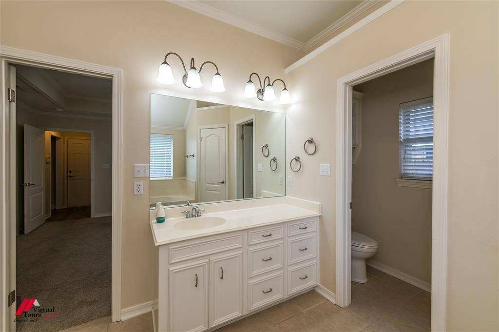 Bathroom featuring a white vanity cabinet with an integrated sink, a large frameless mirror, dual wall-mounted light fixtures, and ceramic tile flooring