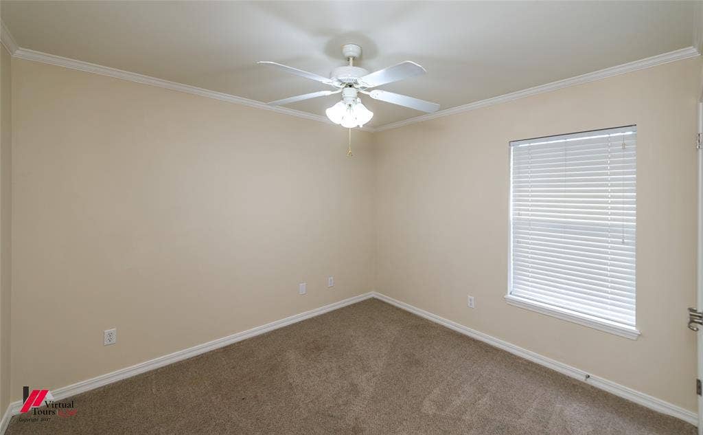 Neutral-toned interior featuring wall-to-wall carpeting, crown molding, a ceiling fan with integrated light fixture, and a window with horizontal blinds