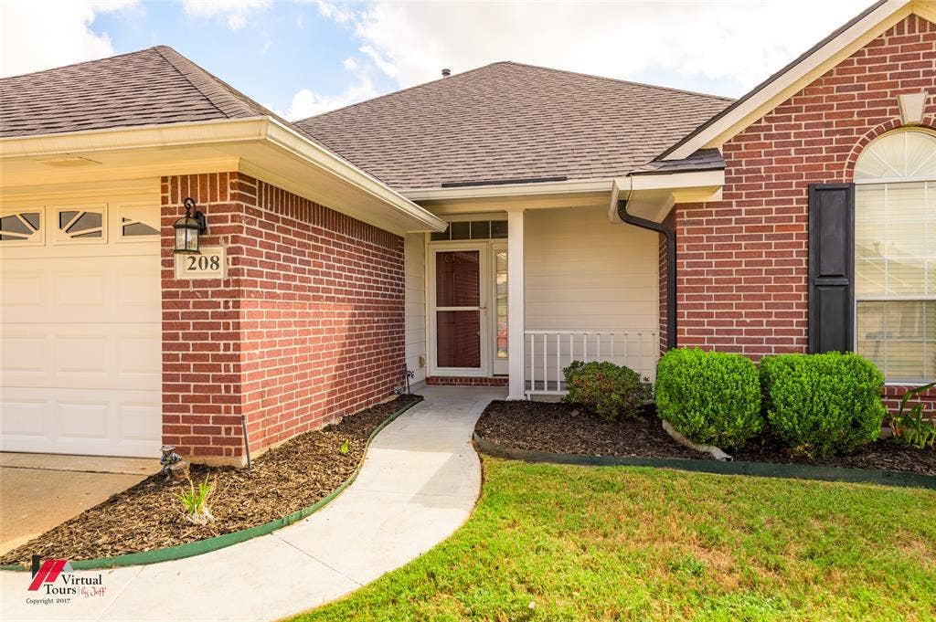 Red brick facade with a covered entryway, shingled roof, attached garage, and arched window