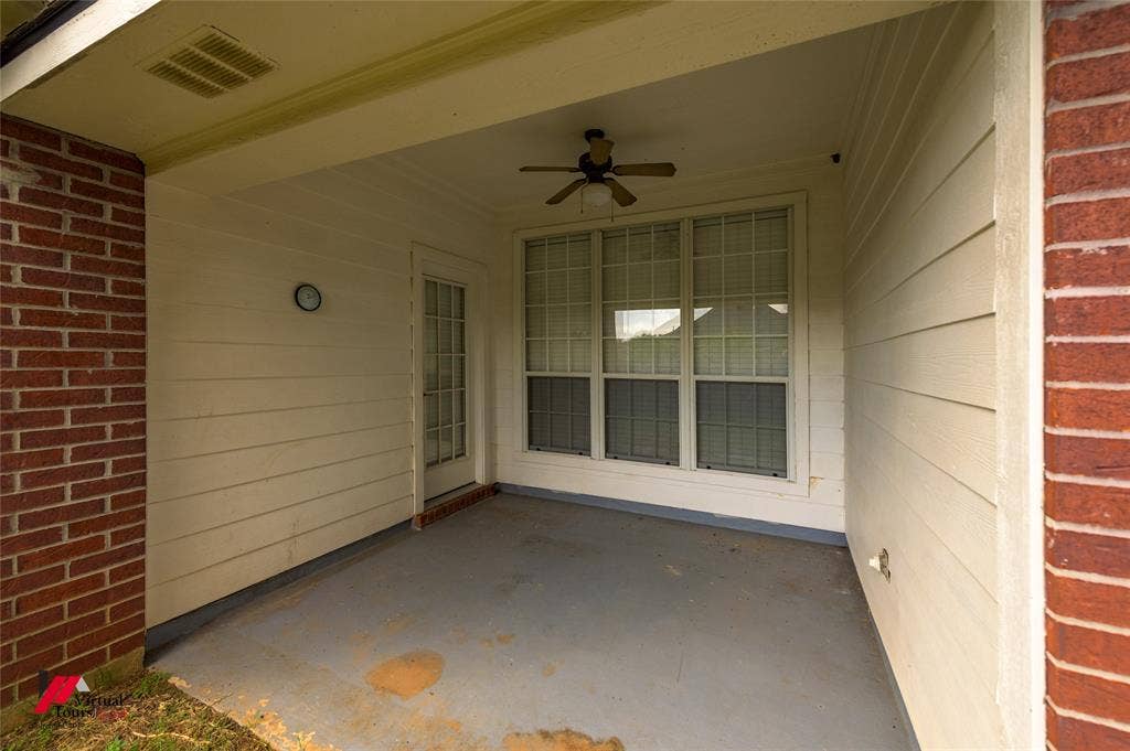 Covered patio featuring red brick siding, horizontal composite siding, a multi-pane glass door, and an overhead ceiling fan