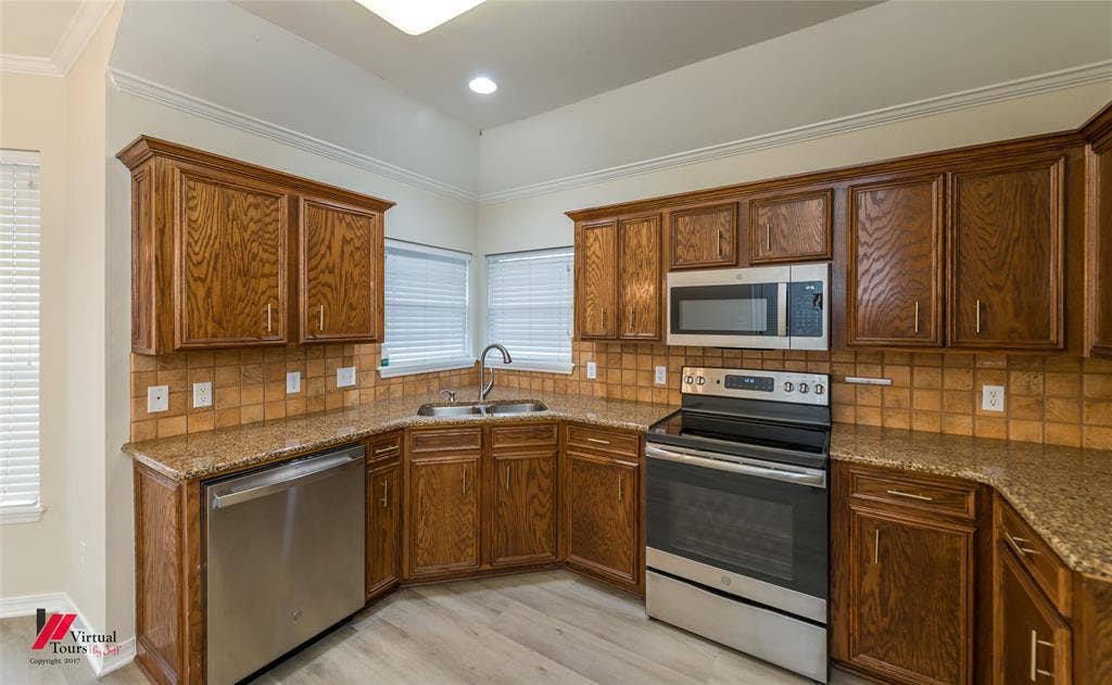 Kitchen featuring stained wood cabinetry, stone-finish countertops, stainless steel appliances, and tile backsplash