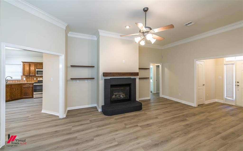 Living area featuring high ceilings with crown molding, wood-finish flooring, a central fireplace with a dark tile surround and wood mantel, and built-in wall shelving