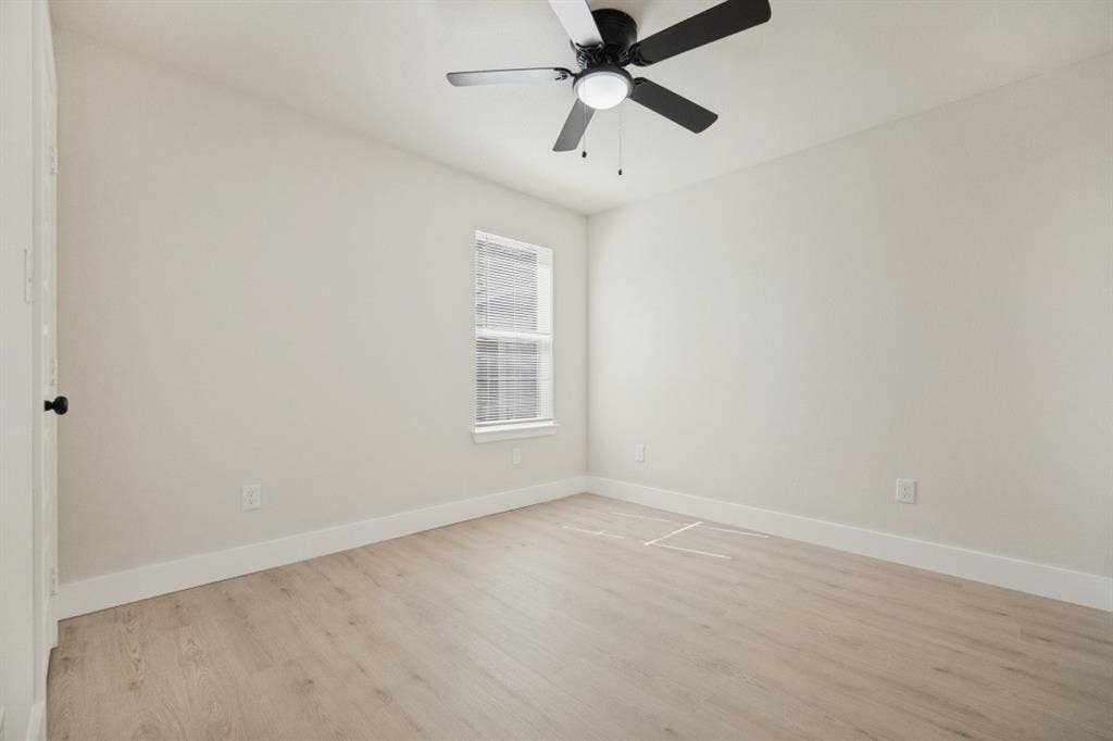 Light-toned wood-finish flooring with white baseboards, a window with horizontal blinds, and a ceiling fan with integrated lighting