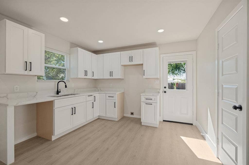 Modern kitchen featuring white shaker-style cabinetry, light-toned wood-finish flooring, recessed lighting, white countertops, and a black gooseneck faucet