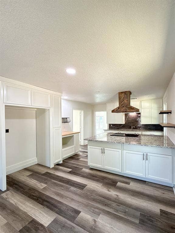 150 Fm 1996, Oglesby, TX 76561 Kitchen featuring wood-finish flooring, white cabinetry, a central island with a light-toned countertop, a dark tile backsplash, and a wood-finish range hood