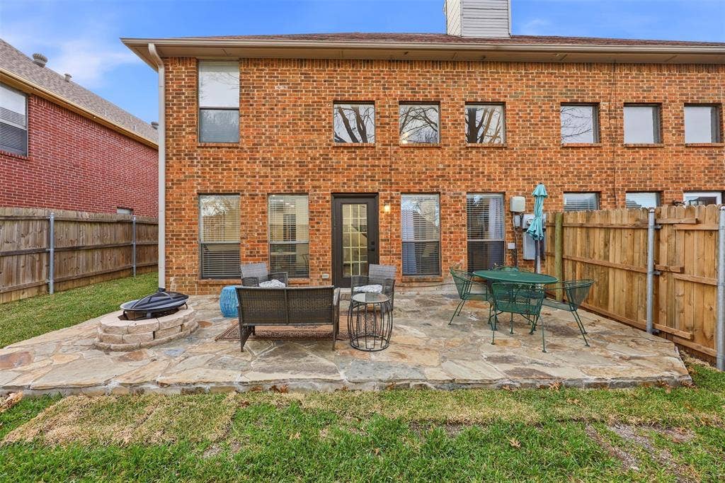 Red brick exterior with multiple windows, leading to a stone patio with a built-in fire pit