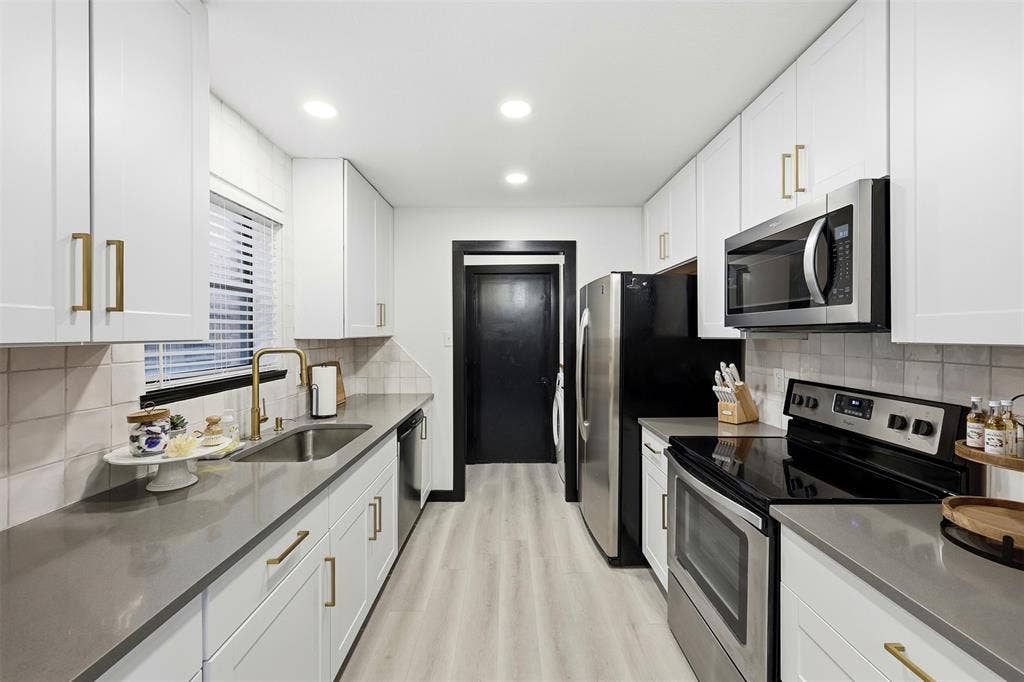 Galley kitchen featuring white cabinetry, gold-tone hardware, stainless steel appliances, a gold-tone faucet, and light wood-finish flooring