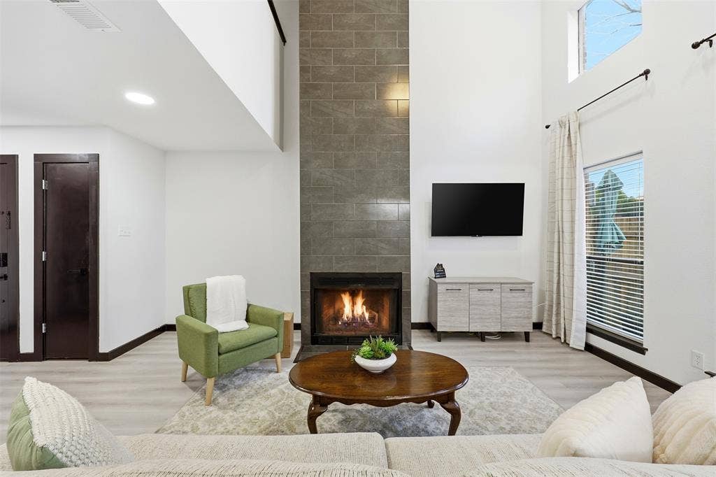 Soaring ceilings, a floor-to-ceiling tiled fireplace, and light wood-finish flooring define this living space