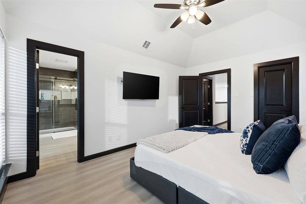 Vaulted ceiling with a ceiling fan, light wood-finish flooring, and dark trim doors