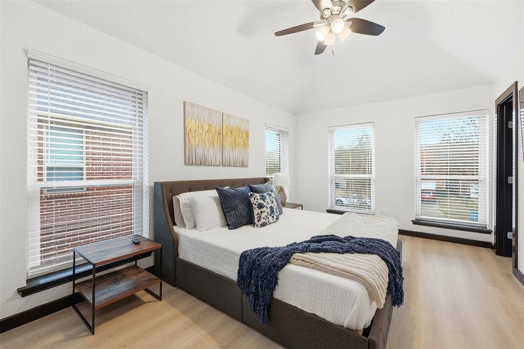 Vaulted ceiling with a ceiling fan, three windows with blinds, light wood-finish flooring, and white walls