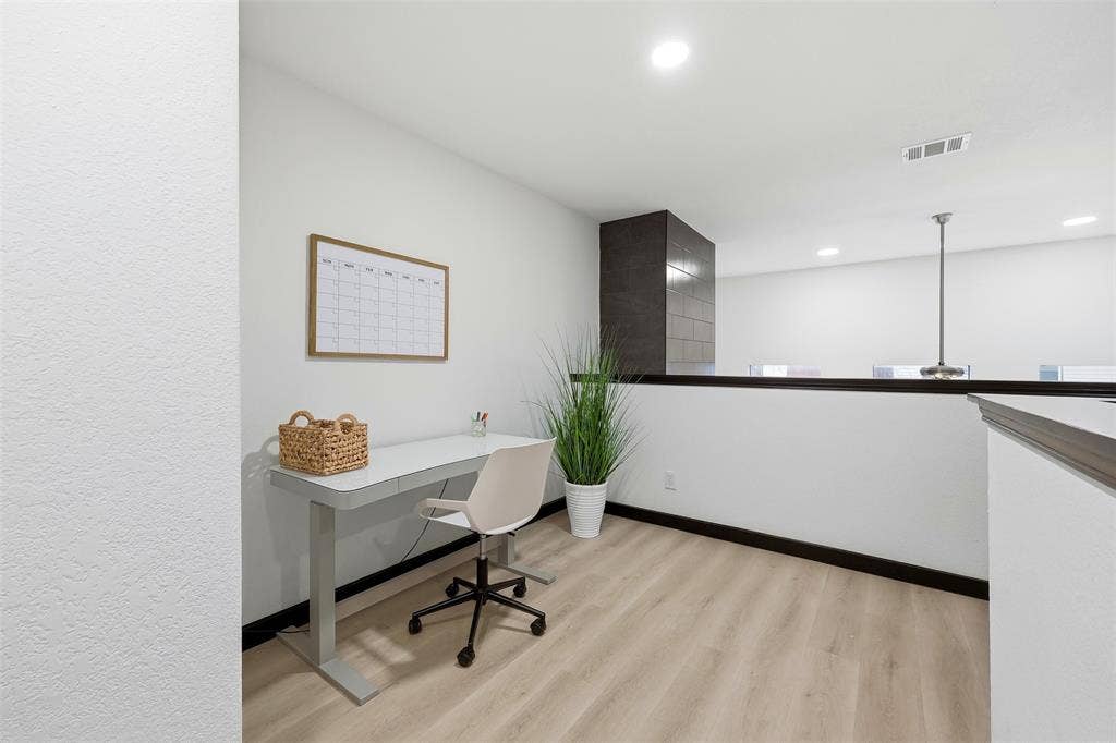 Light wood-finish flooring, recessed ceiling lighting, and a dark tile-clad architectural element
