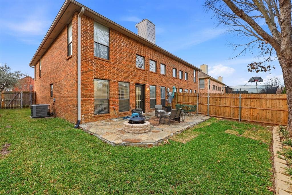 Brick exterior with multiple windows, featuring a flagstone patio with a built-in fire pit, surrounded by a wooden privacy fence and a grassy yard