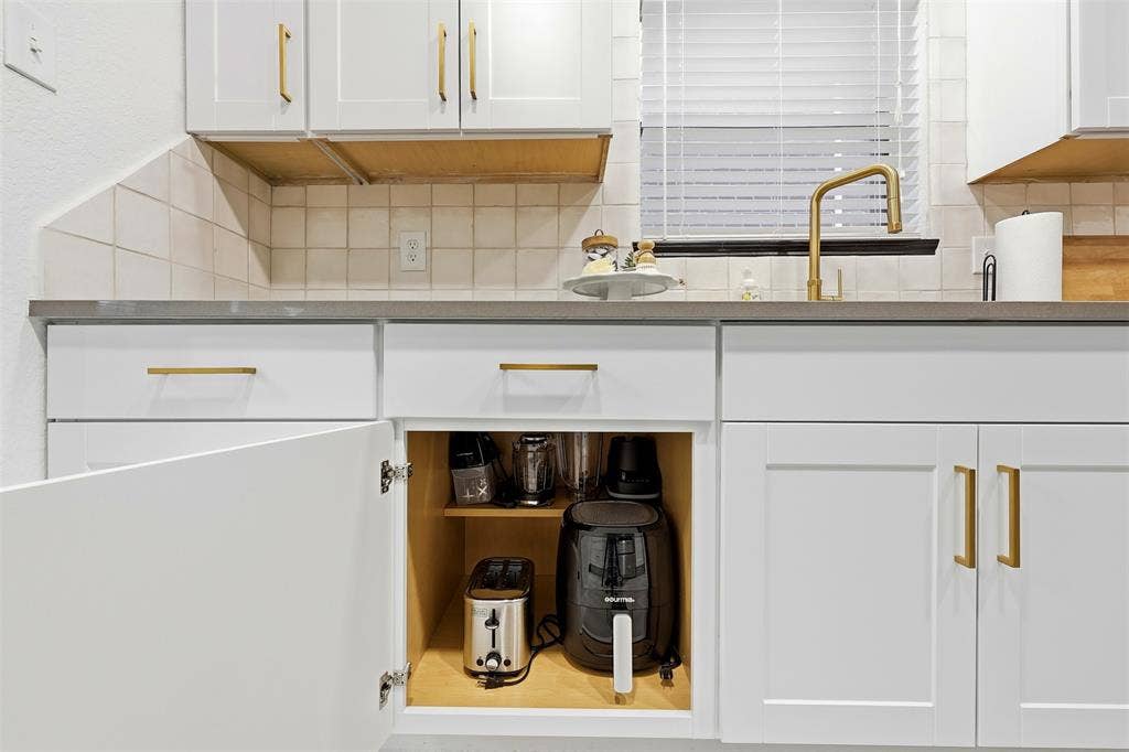White cabinetry with gold-tone hardware, solid surface countertops, and a gold-tone gooseneck faucet