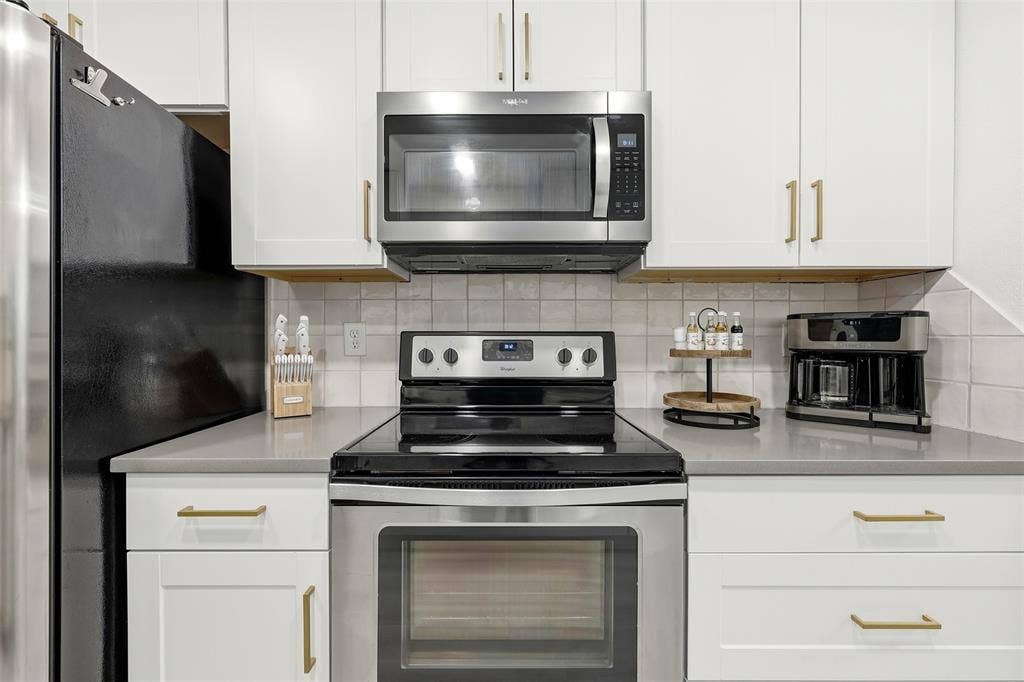 White cabinetry with gold-tone hardware, stainless steel appliances, and light-toned countertops