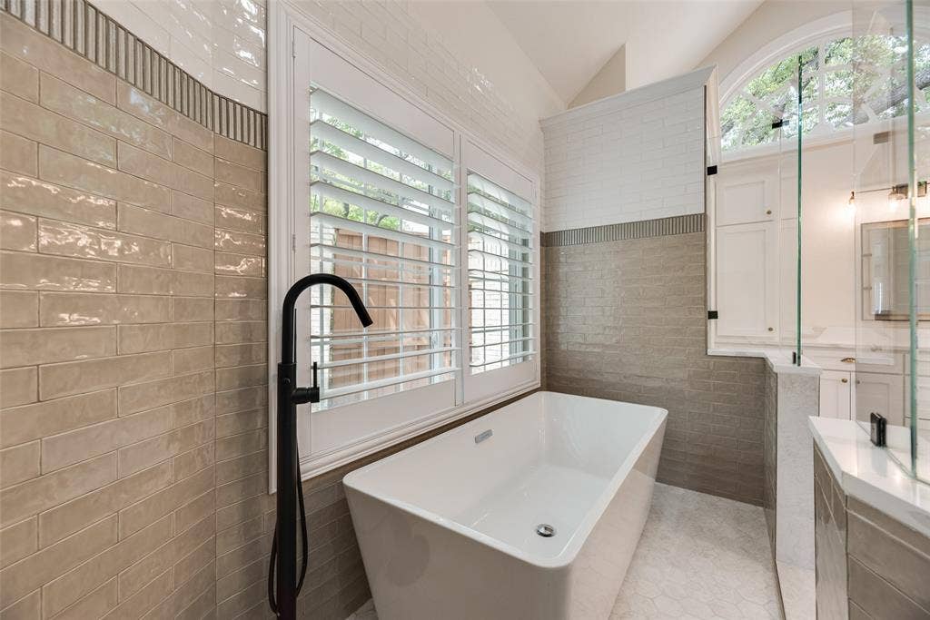 4612 Saxon Drive, Plano, TX 75093 Freestanding soaking tub with a floor-mounted matte black faucet, plantation shutters, and a frameless glass shower enclosure