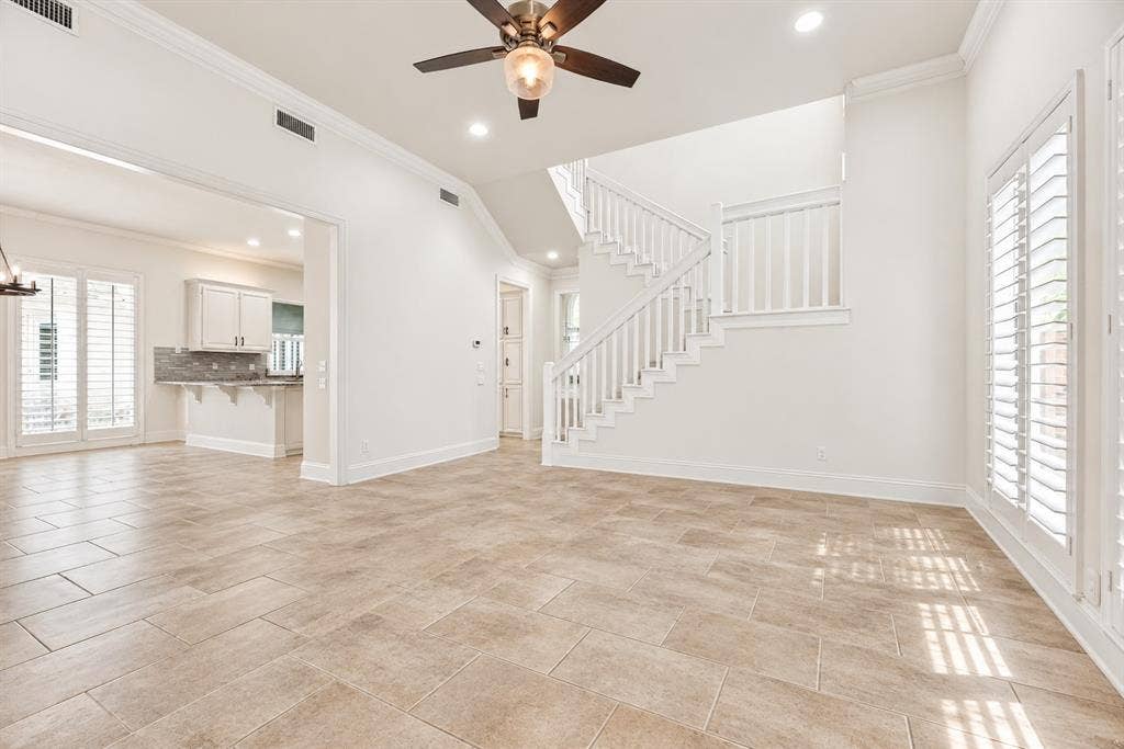 4612 Saxon Drive, Plano, TX 75093 Open-concept living space featuring tiled flooring, a prominent staircase with white railings, and white plantation shutters on large windows