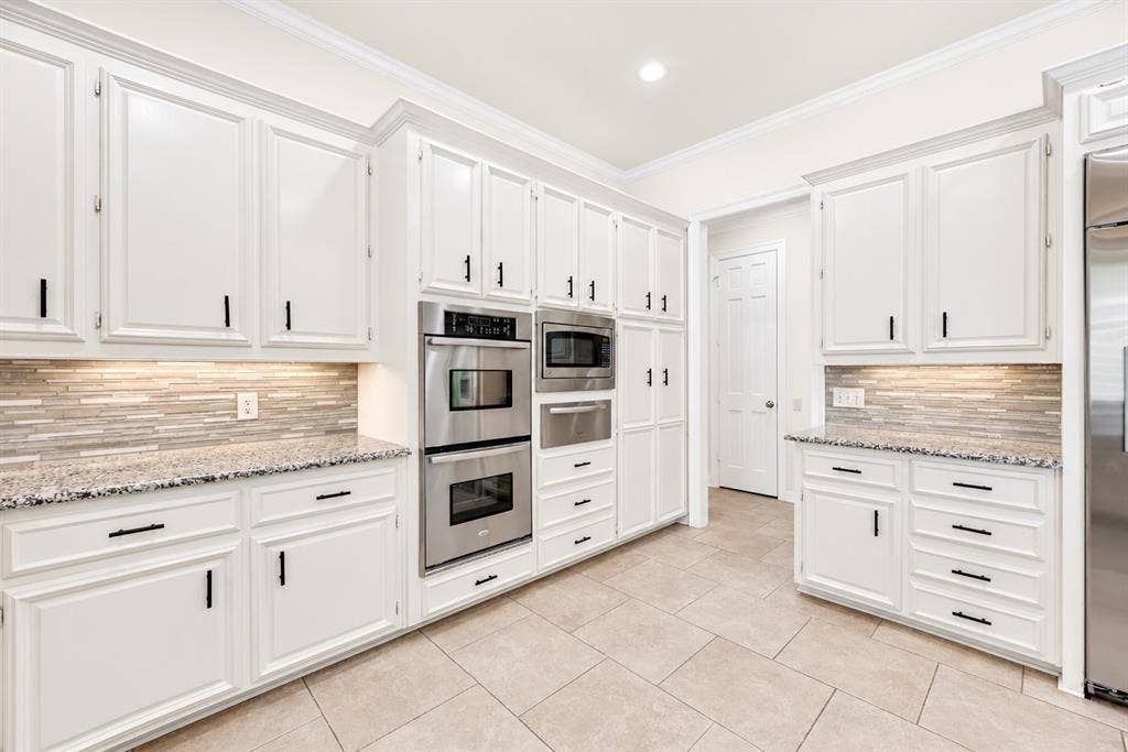 4612 Saxon Drive, Plano, TX 75093 White cabinetry, granite countertops, stainless steel double oven, microwave, and tile flooring