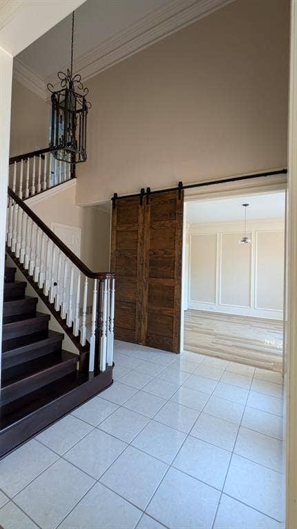 Two-story foyer featuring a dark wood-finish staircase with white balusters, square tile flooring, a decorative iron chandelier, and wood-finish barn doors leading to an additional room with a pendant light