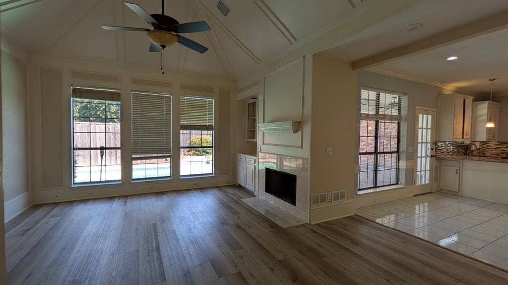 Vaulted ceiling with decorative trim, wood-finish flooring, built-in fireplace with mantel, built-in cabinetry, and large windows overlooking the pool