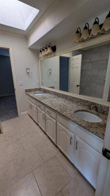Dual vanity with integrated sinks, granite countertop, white cabinetry, and tile flooring