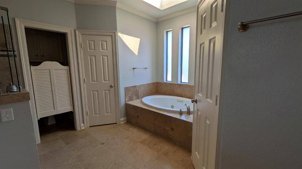 Recessed jetted tub with a tiled surround, two vertical window features, and a skylight