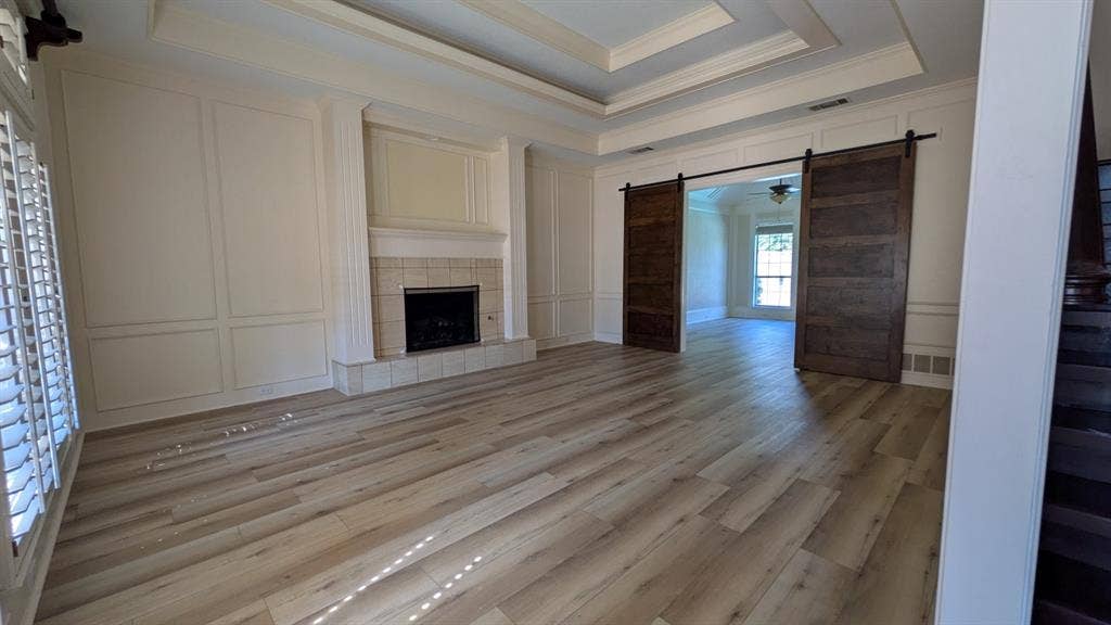 Wood-finish flooring, coffered ceiling, fireplace with tile surround, paneled accent wall, and sliding barn doors